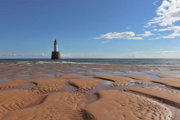 istock Lighthouse near beach with grooves in sand under blue sky with fluffy white clouds 1040337586