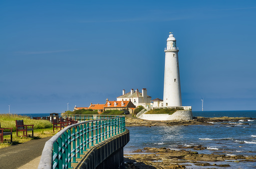 A view of St Mary's Lighthouse, Whitley Bay, Tyne and Wear on a sunny day, with the curved promenade and fence in the foreground
