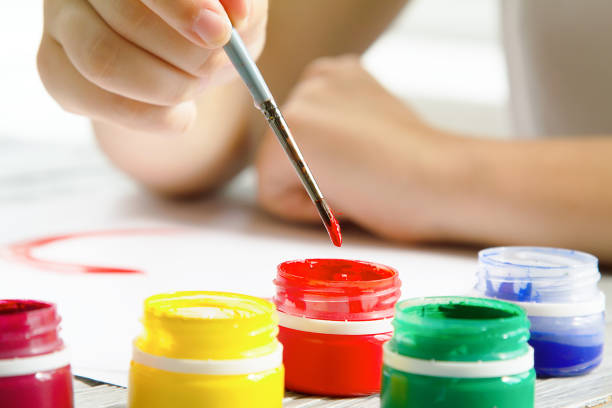 close-up of hand with brush and paints on a wooden table at home