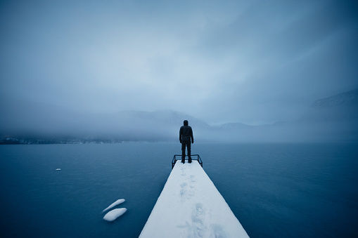 Peaceful winter morning by the frozen lake. Man is standing on the pier.