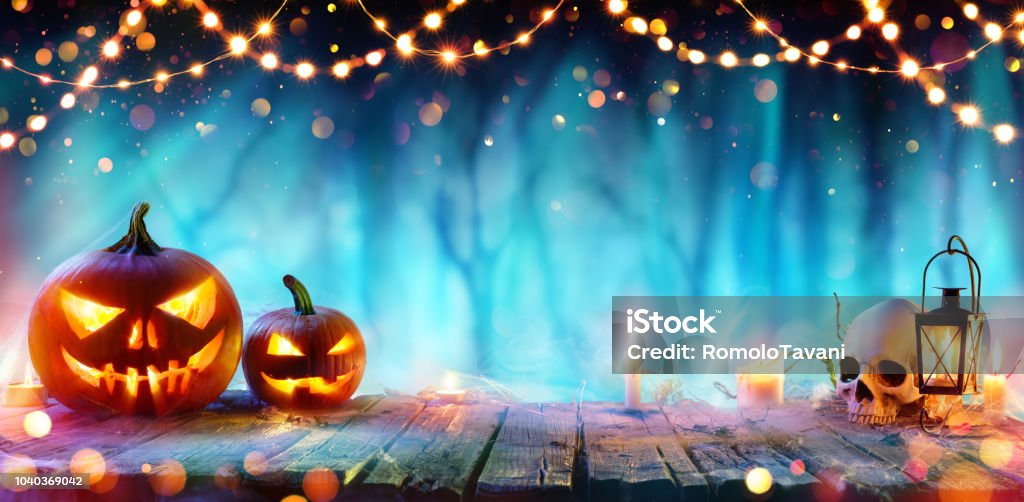 Halloween Party - Jack O' Lanterns And String Lights On Table In Misty Forest Pumpkins And Skull On Table At Dust In Forest Halloween Stock Photo