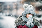 Teenage girl blowing nose on winter day