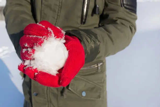 closeup of hands in red gloves holding snowball in winter outdoors