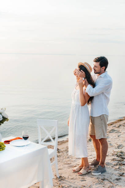 istock young man closing eyes and making surprise for girlfriend, romantic date on beach 1040386524