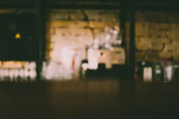 Photo of Blurred defocused interior of a craft beer pub. View from the vintage wooden counter. Bricked wall on the background. Popular place to drink with friends on Friday evenings.