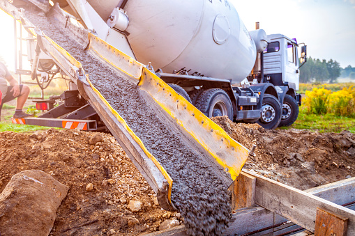 Pouring concrete to the foundations of the building. Construction Worker Guiding Cement Mixer Truck Trough. Cement Pouring from a Mixer Truck Chute. Concrete Foundation Construction.