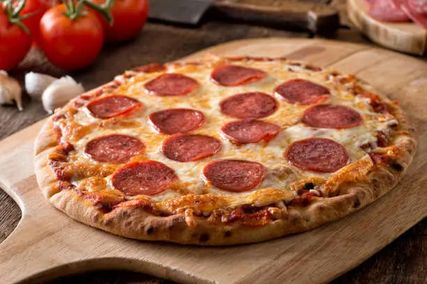 A delicious fresh homemade pepperoni pizza on a wooden pizza pull.