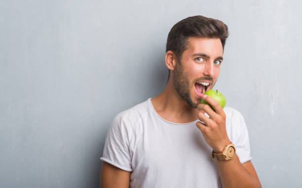 istock Handsome young man over grey grunge wall eating green apple with a confident expression on smart face thinking serious 1040433082