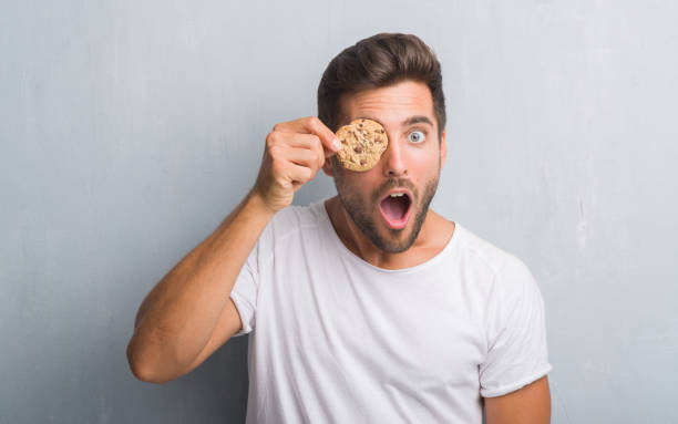 istock Handsome young man over grey grunge wall eating chocolate chip cooky scared in shock with a surprise face, afraid and excited with fear expression 1040434730