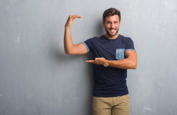 istock Handsome young man over grey grunge wall gesturing with hands showing big and large size sign, measure symbol. Smiling looking at the camera. Measuring concept. 1040440190