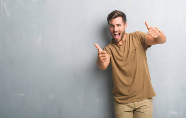 istock Handsome young man over grey grunge wall approving doing positive gesture with hand, thumbs up smiling and happy for success. Looking at the camera, winner gesture. 1040441418