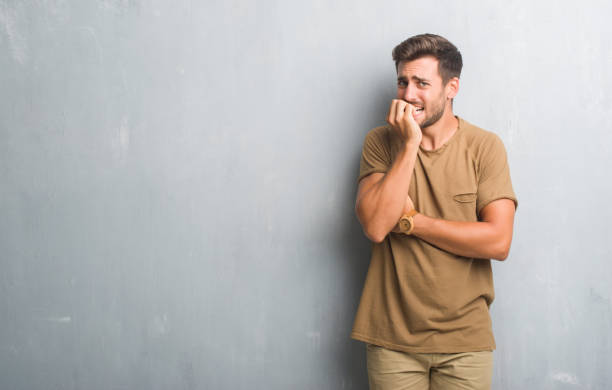 istock Handsome young man over grey grunge wall looking stressed and nervous with hands on mouth biting nails. Anxiety problem. 1040441450