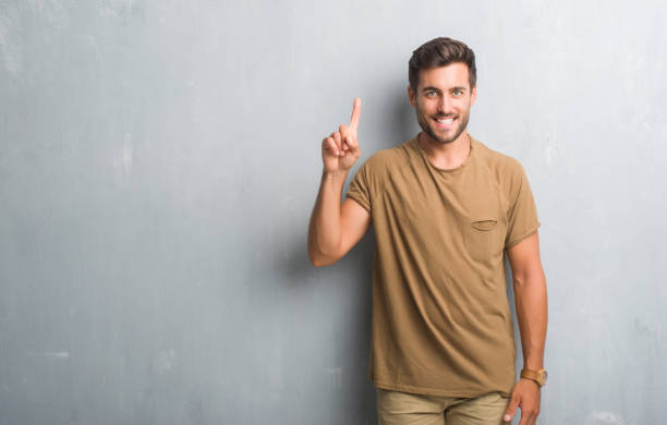 istock Handsome young man over grey grunge wall showing and pointing up with finger number one while smiling confident and happy. 1040441478