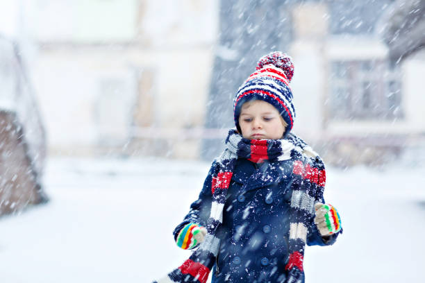 istock Funny little kid boy in colorful clothes playing outdoors during strong snowfall 1040444220