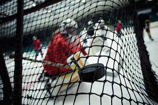 Rear view of a ice hockey net with a puck hitting the back of the net. The focus is on the foreground on the puck, scoring a goal.