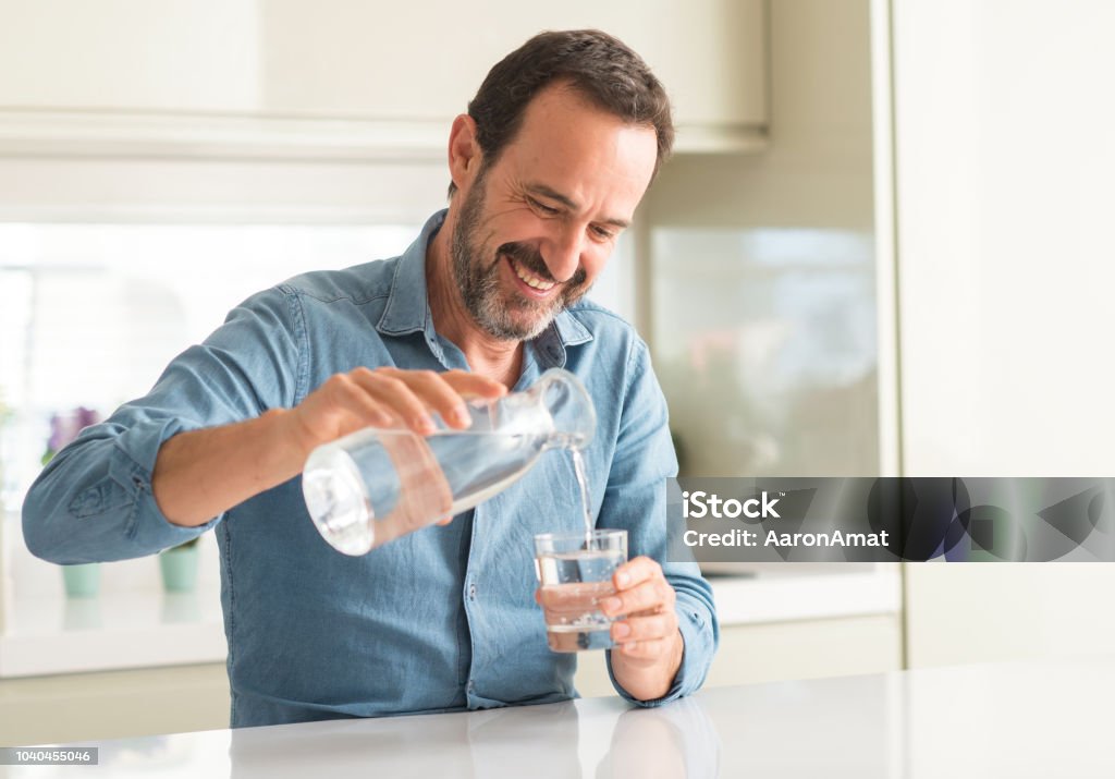 Man van middelbare leeftijd drinken van een glas water met een blij gezicht permanent en lachend met een vertrouwen glimlach weergeven tanden - Royalty-free Water Stockfoto