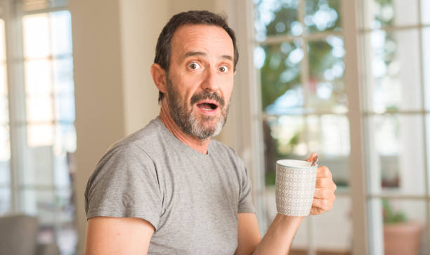 Middle age man drinking coffee in a cup scared in shock with a surprise face, afraid and excited with fear expression