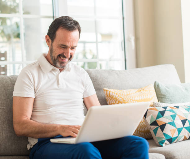 istock Middle age man using laptop at sofa with a happy face standing and smiling with a confident smile showing teeth 1040459122
