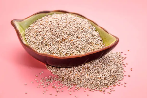 white chia seeds in a leaf shaped ceramic bowl against pink background