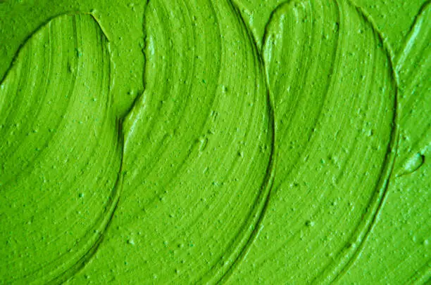 Photo of Green cosmetic clay (facial mask, cream) texture close up, selective focus. Abstract lime green background with brush strokes.