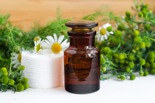 Pharmacy bottle with cosmetic/cleansing/healing wild chamomile aroma oil or tincture and cotton pads for natural skin care and medicinal purposes. Homemade cosmetics and phytotherapy.