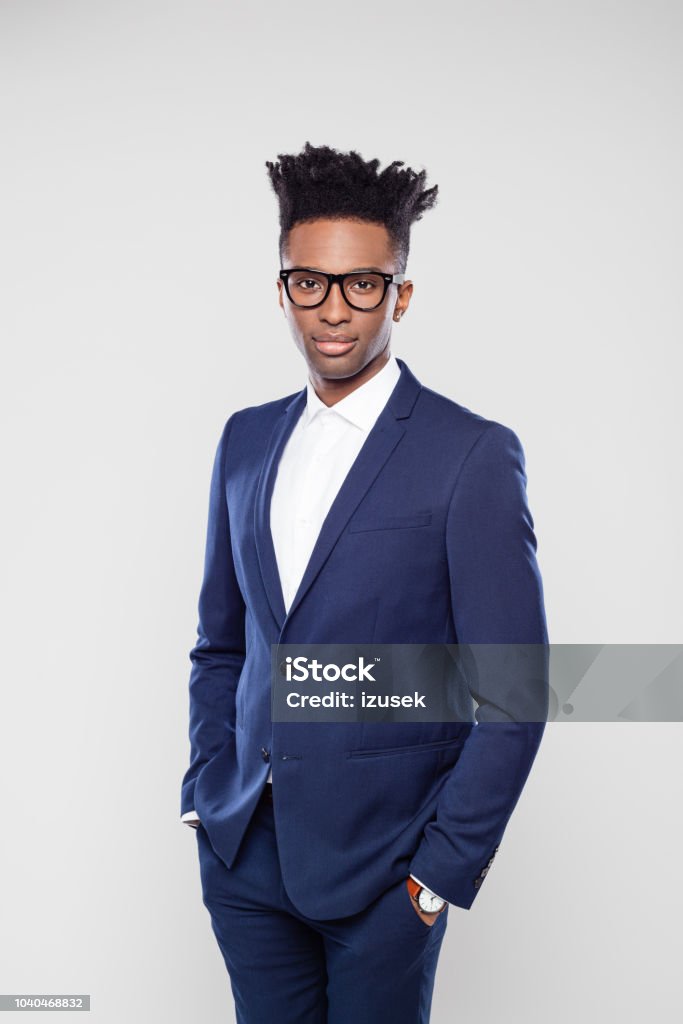 Handsome afro american businessman in studio Portrait of handsome afro american businessman standing with his hands in pocket on white background. African guy in business suit wearing eyeglasses staring at camera confidently in studio. Men Stock Photo