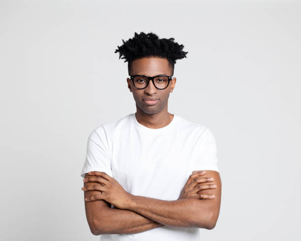 Nerdy staring at camera Portrait of handsome afro american man standing with arms crossed looking at camera. Man in white t-shirt wearing eyeglasses with funky hairstyle. black nerd stock pictures, royalty-free photos & images