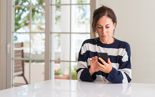 Middle aged woman using smartphone with a confident expression on smart face thinking serious