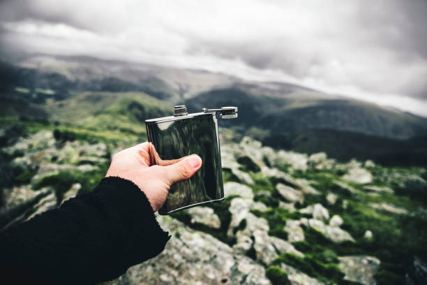 A man's hand holding a flask A man's hand holding a flask on a background of rocks and green hills. hipflask stock pictures, royalty-free photos & images