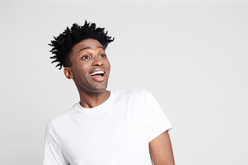 Close up portrait of afro american man with surprised expression, looking away at copy space with mouth open on white background