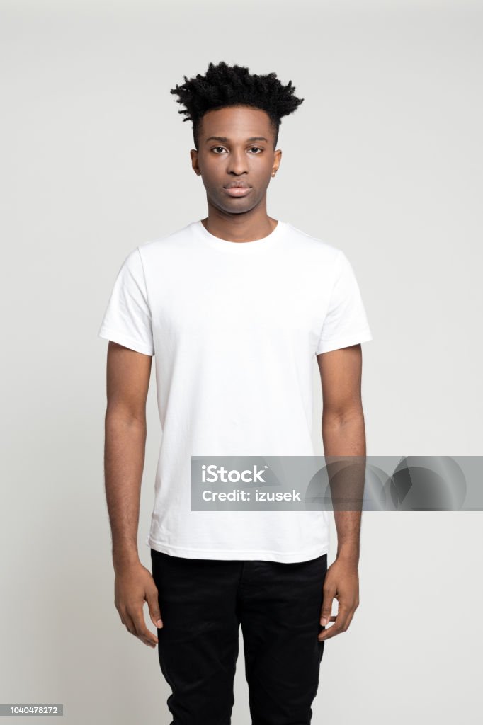 Serious young afro american man standing in studio Studio portrait of serious young afro american man standing on white background. African male in white t-shirt staring at camera. T-Shirt Stock Photo
