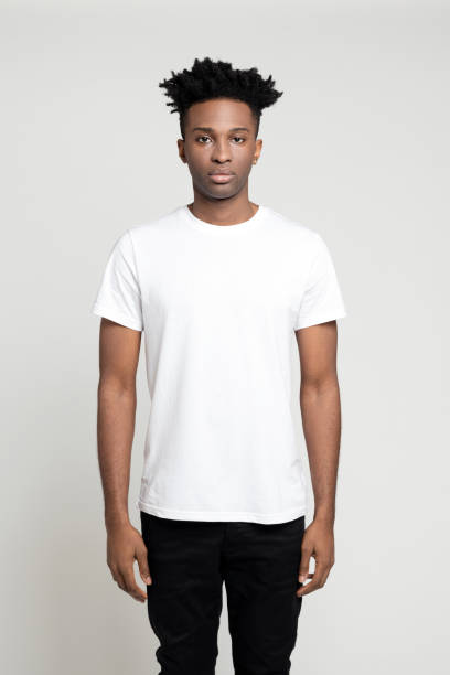 Serious young afro american man standing in studio Studio portrait of serious young afro american man standing on white background. African male in white t-shirt staring at camera. no emotion stock pictures, royalty-free photos & images