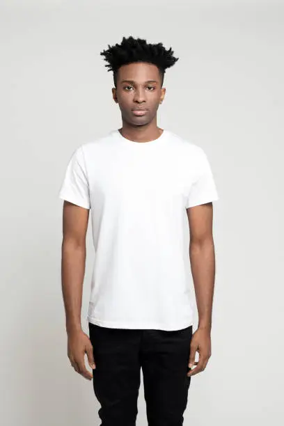 Studio portrait of serious young afro american man standing on white background. African male in white t-shirt staring at camera.