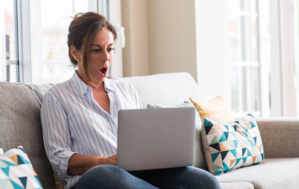 istock Middle aged woman using laptop in the sofa scared in shock with a surprise face, afraid and excited with fear expression 1040480890