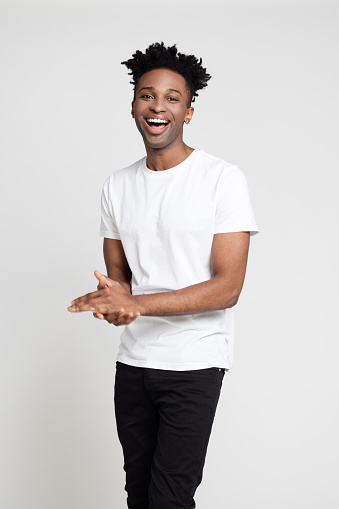 Portrait of handsome young man in causals laughing on white background. Afro american male model in white t-shirt and black jeans looking at camera and smiling in studio.
