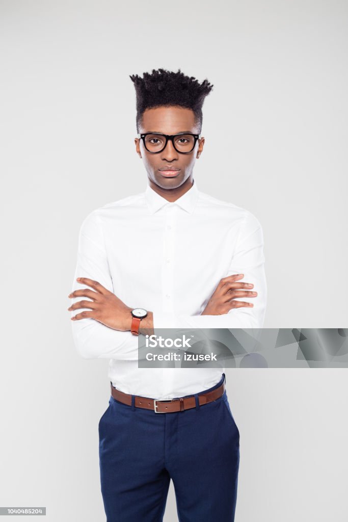 Afro american businessman staring at camera Portrait of young afro american businessman standing with his arms crossed staring at camera on white background. Button Down Shirt Stock Photo