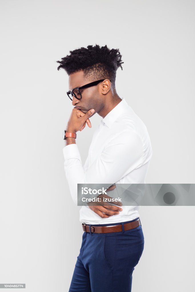 Stressed businessman thinking of solution Side portrait of young african businessman thinking with his eyes closed and hand on chin. Stressed man thinking of solution using mindfulness. Business Person Stock Photo