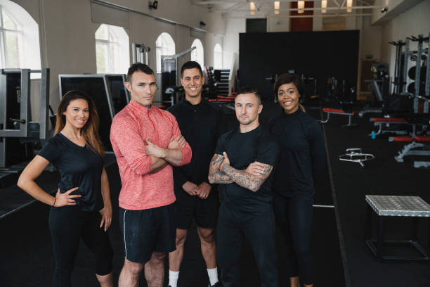Five personal trainers are standing in the gym in their uniforms, looking at the camera.