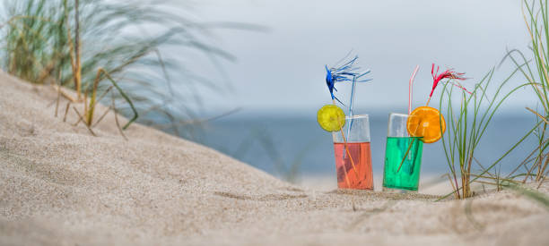 모래 해변에서 marram 잔디 사이 두 개의 장미와 녹색 레모네이드 안경 - beach sand drink drink umbrella 뉴스 사진 이미지