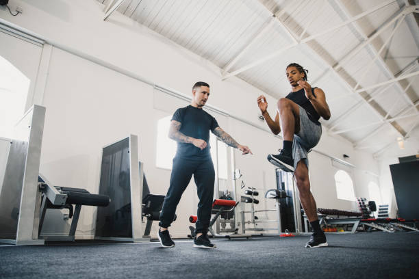 Warm Up Movement Exercises Young man performing warm up movement exercises in the gym. His personal trainer is right beside him for guidance. fitness trainer stock pictures, royalty-free photos & images