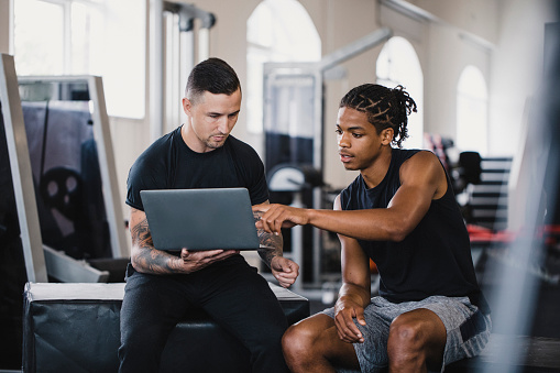 Personal trainer and a client sitting in a gym discussing the clients fitness progress.