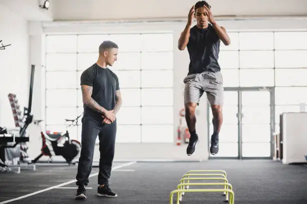 Young man having a personal training session in the gym. He is doing warm up exercises while his personal trainer guides him.