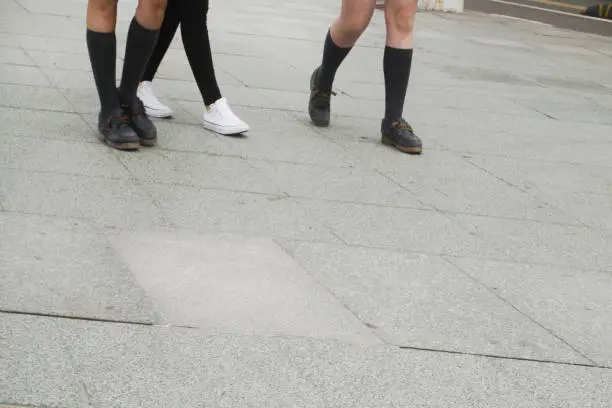 Photo of Detail of girls' legs wearing school uniforms on stone paved street.