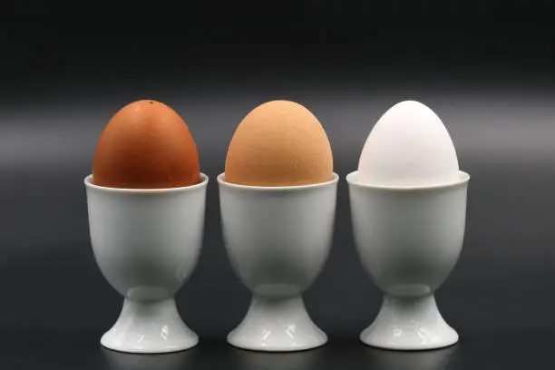brown to white three breakfast eggs in eggcup isolated on black