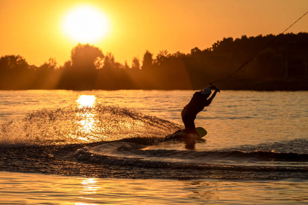 wake board un uomo fa un trucco al tramonto sul tabellone sugli schizzi d'acqua - wakeboarding surfing men vacations foto e immagini stock