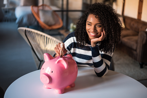 Black young woman with pink saving piggy bank