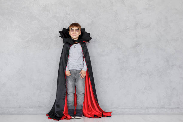Halloween vampire boy Smiling boy with vampire makeup and black, red cloak with bat like collar on a gray textured background. Halloween mood, copy space available. Cute kid wearing halloween costume. face paint halloween adult men stock pictures, royalty-free photos & images
