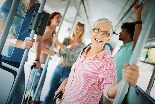 Closeup of group of random people riding a local city bus. There are some seniors and young adults, a senior lady with short gray hair is smiling to the camera while the rest are riding the bus quietly.