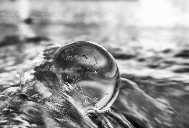 Glass ball being wrapped by ocean wave in black and white close up