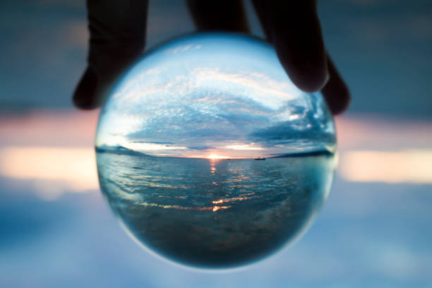 Sunset seascape captured in clear glass ball held in fingers